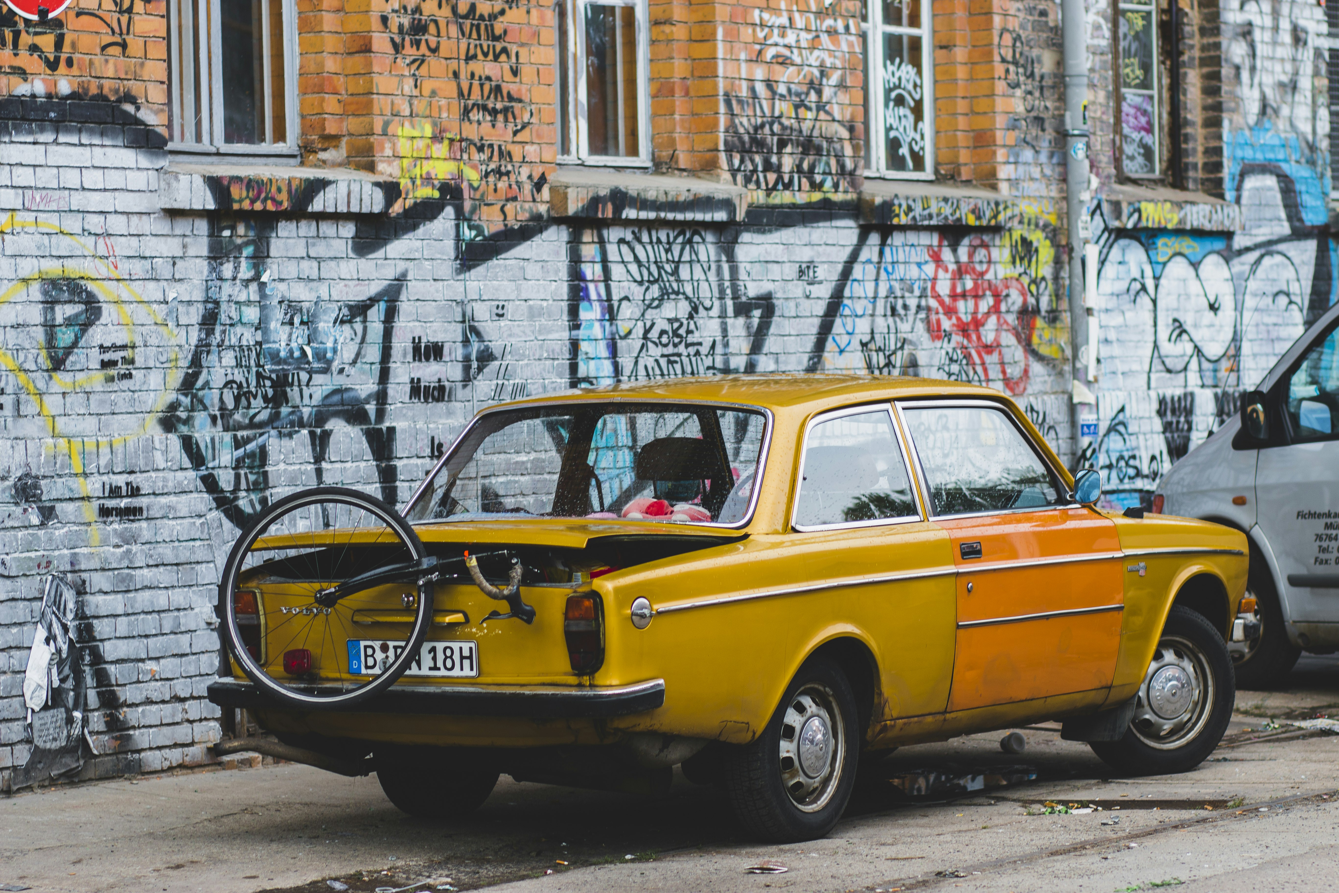 vintage yellow coupe with unicycle on back park near graffiti wall